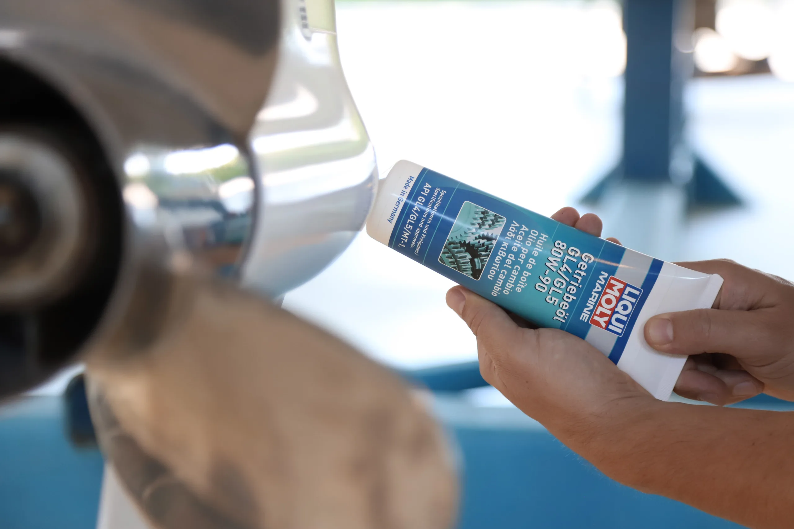 Mann befüllt das Getriebe eines weißen Außenbordmotors mit Liqui Moly Getriebeöl aus einer Tube.
