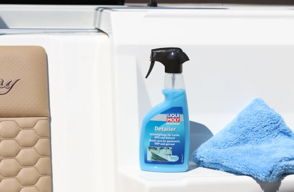 Eine Sprühflasche mit Reiniger und ein Mikrofasertuch stehen auf einer weißen gepolsterten Sitzbank eines Boots.
